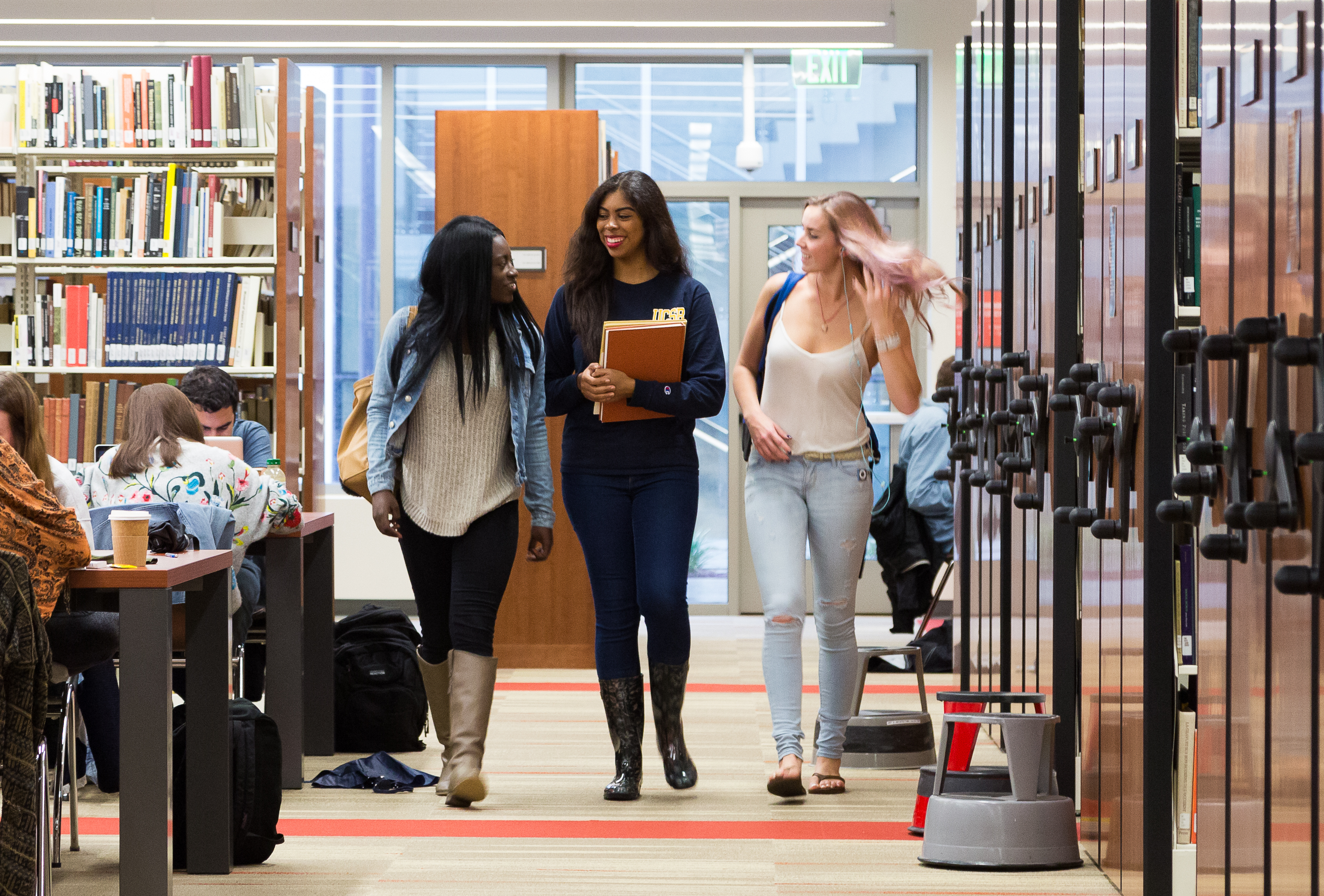 three students walking in the library